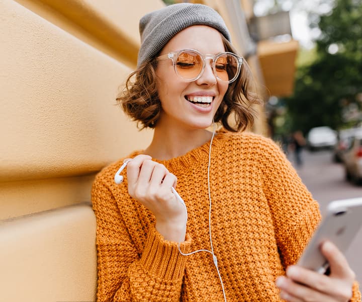 Charming short haired lady gray hat standing beside wall with smartphone